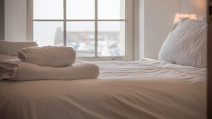 A neatly made bed with white linens and two folded towels on the left side.