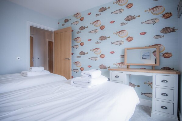 A bedroom with two beds, a wooden desk, and a wall with fish patterns.
