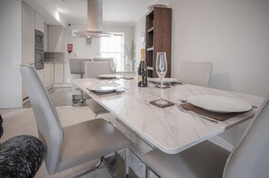 Un comedor moderno con una mesa de mármol, sillas blancas y una cocina al fondo.