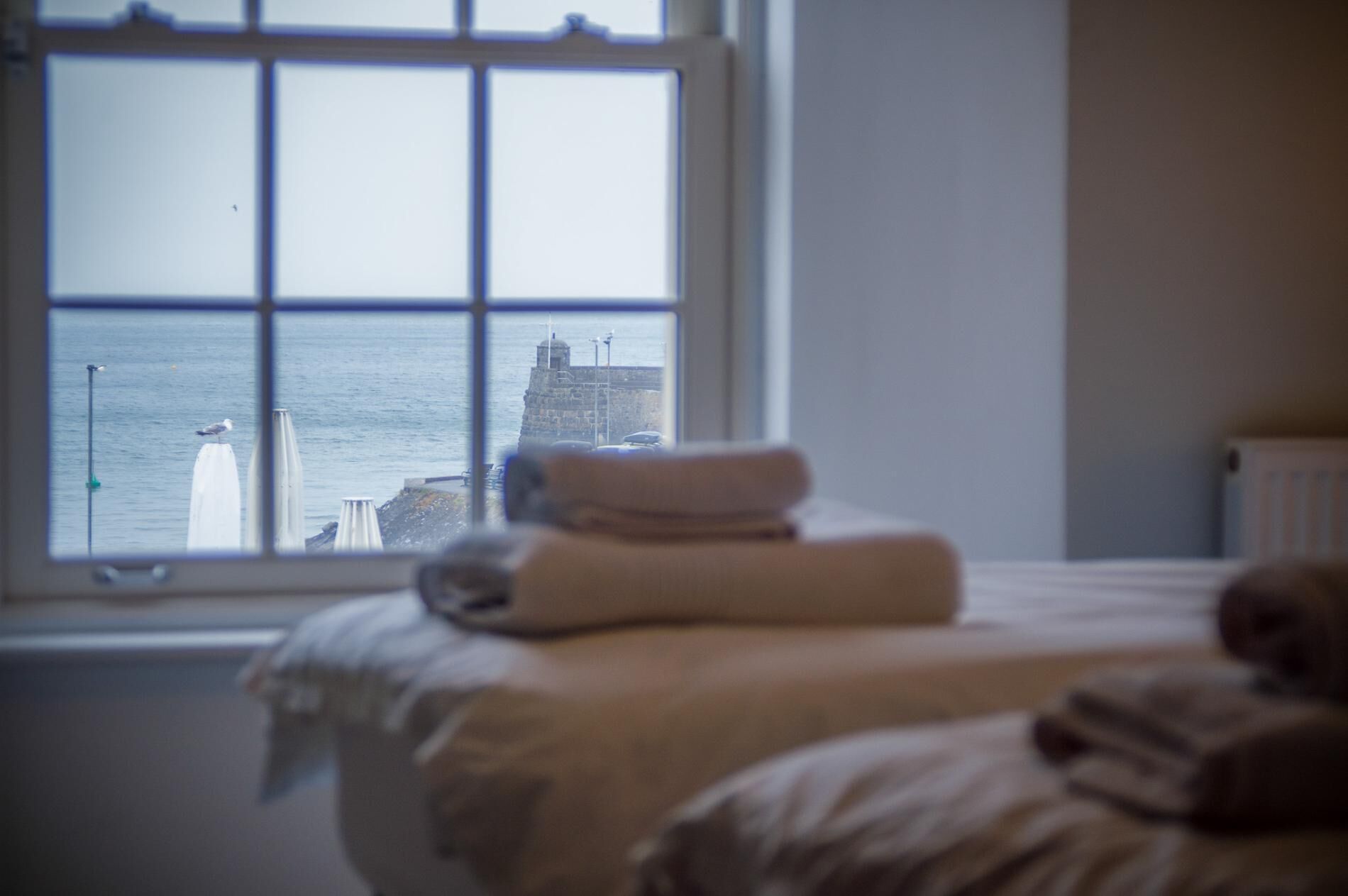 A bedroom with a bed, a window, and a view of a lighthouse and sea.