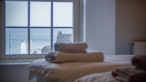 A bedroom with a bed, a window, and a view of a lighthouse and sea.