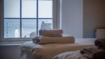 A bedroom with a bed, a window, and a view of a lighthouse and sea.
