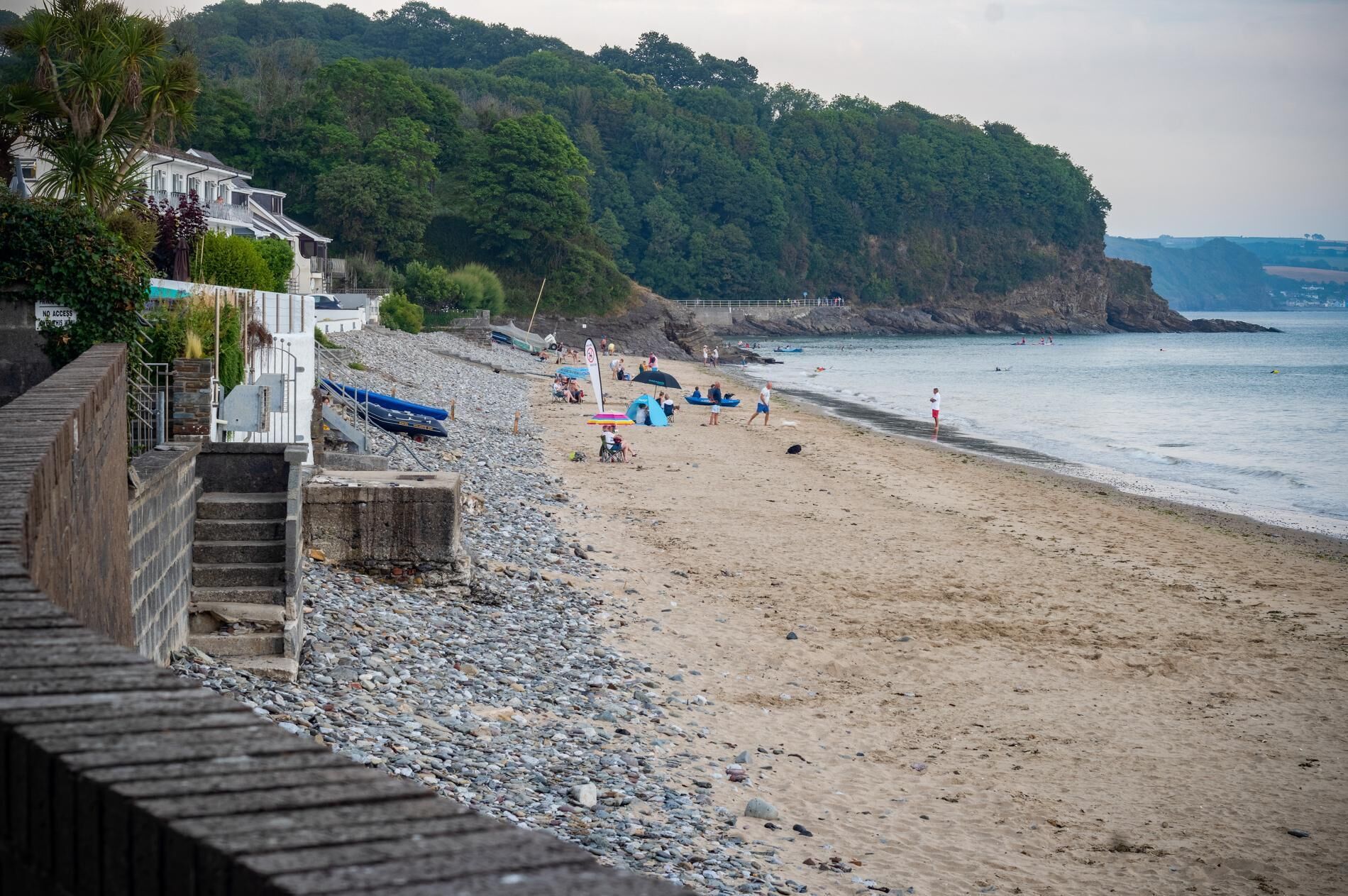 A beach with a rocky shoreline, a wooden staircase leading down to the beach, and a building with a balcony overlooking the beach.