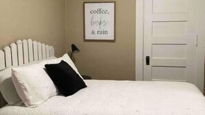 Un dormitorio con una cama, una puerta blanca y un cartel en la pared que dice 'coffee, books & rain'.