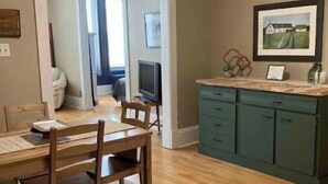 Un comedor con mesa y sillas de madera, una cocina con armarios verdes y un pasillo que conduce a otra habitación.