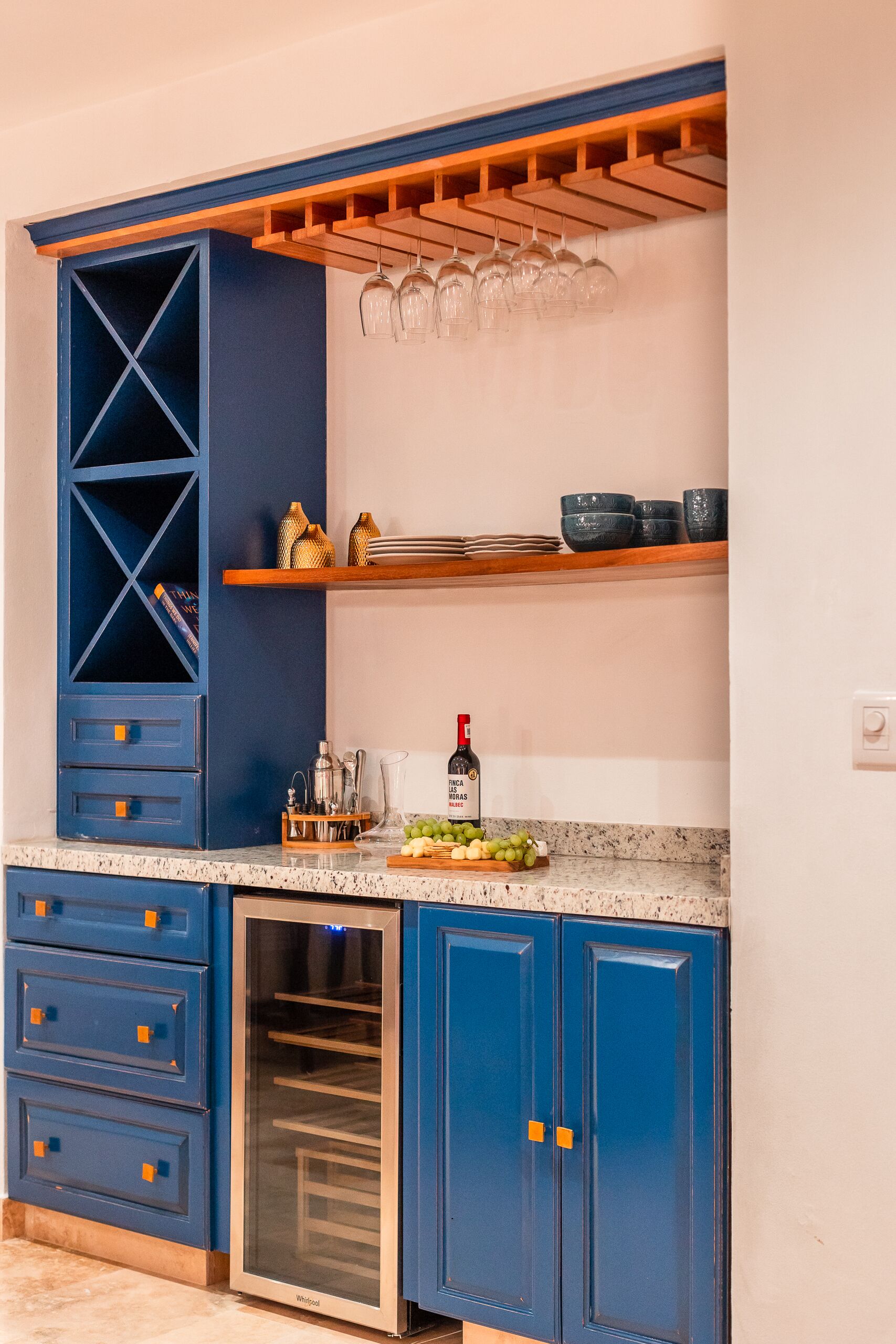 A kitchen with blue cabinets, a wine cooler, and a wooden shelf with glasses.