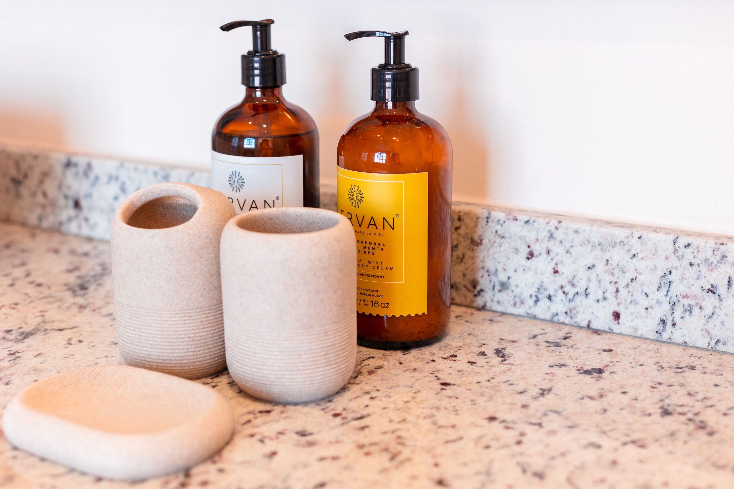 Two brown bottles with pump dispensers and a pair of beige ceramic cups on a speckled countertop.