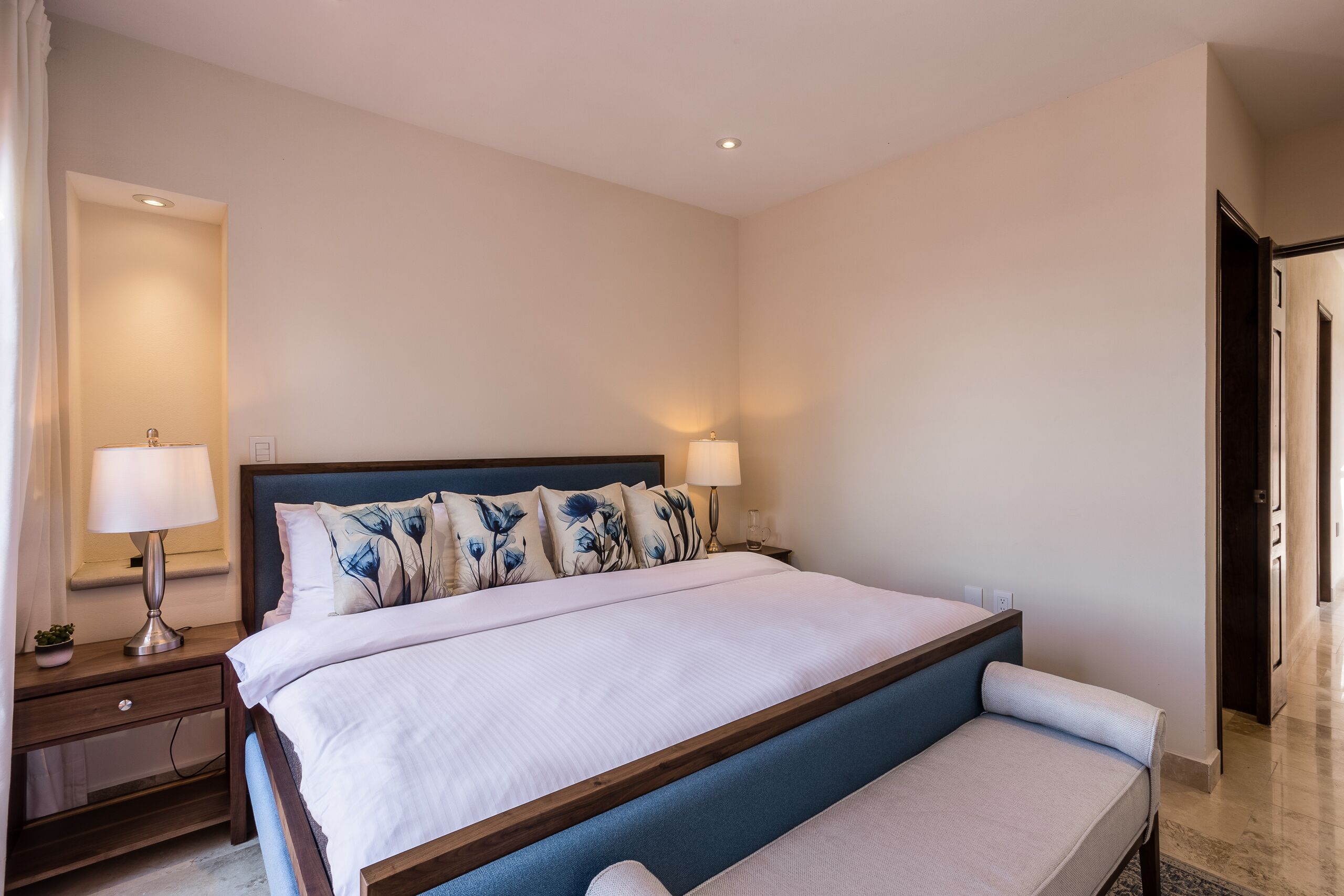 Una camera d'albergo con un letto grande, lampade sui comodini, un tavolino notte e una panca ai piedi del letto.