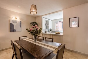 Comedor con mesa de madera, sillas, un florero con flores y una lámpara colgante.