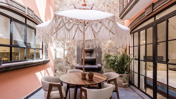 A patio with a round wooden table and chairs, a decorative umbrella, and a stone wall with a fireplace. - Luxury Apartments with Rooftop & Jacuzzi (San Miguel de Allende)