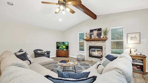 A spacious living room with a fireplace, a ceiling fan, and a large TV.