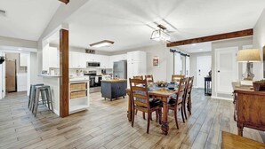 A spacious kitchen with white cabinets, a dining area with wooden chairs, and a visible island with stools.