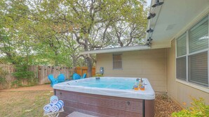 A backyard with a hot tub, a wooden deck, and a wooden fence.
