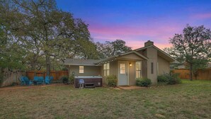 A single-story house with a front yard, a barbecue grill, and a patio with chairs.