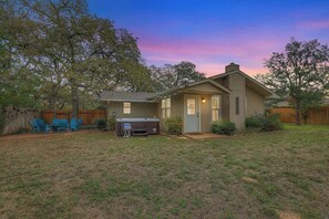 Une maison de plain-pied avec un jardin devant, un barbecue et une terrasse avec des chaises.