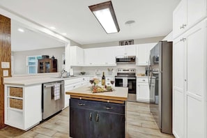 Une cuisine moderne avec des meubles blancs, des appareils en acier inoxydable et un îlot central en bois.