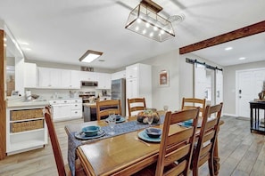 Une cuisine moderne avec des meubles blancs, un coin repas doté d’une table et de chaises en bois, et un luminaire au plafond.