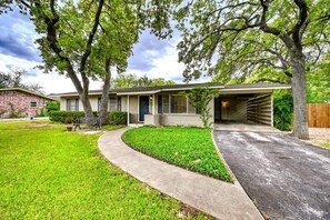 A two-story house with a front garage, a well-maintained lawn, and mature trees. - Billie Goat Haus-HotTub-Near Main St! (Fredericksburg)