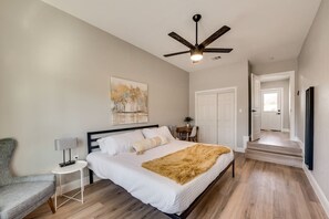 A bedroom with a bed, a chair, a desk, a ceiling fan, and a door leading to another room. - Downtown McKinney Home (McKinney)