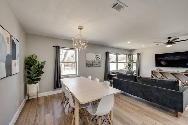 A modern living room with a dining area, a grey sofa, a TV, and a ceiling fan. - Downtown McKinney Home (McKinney)