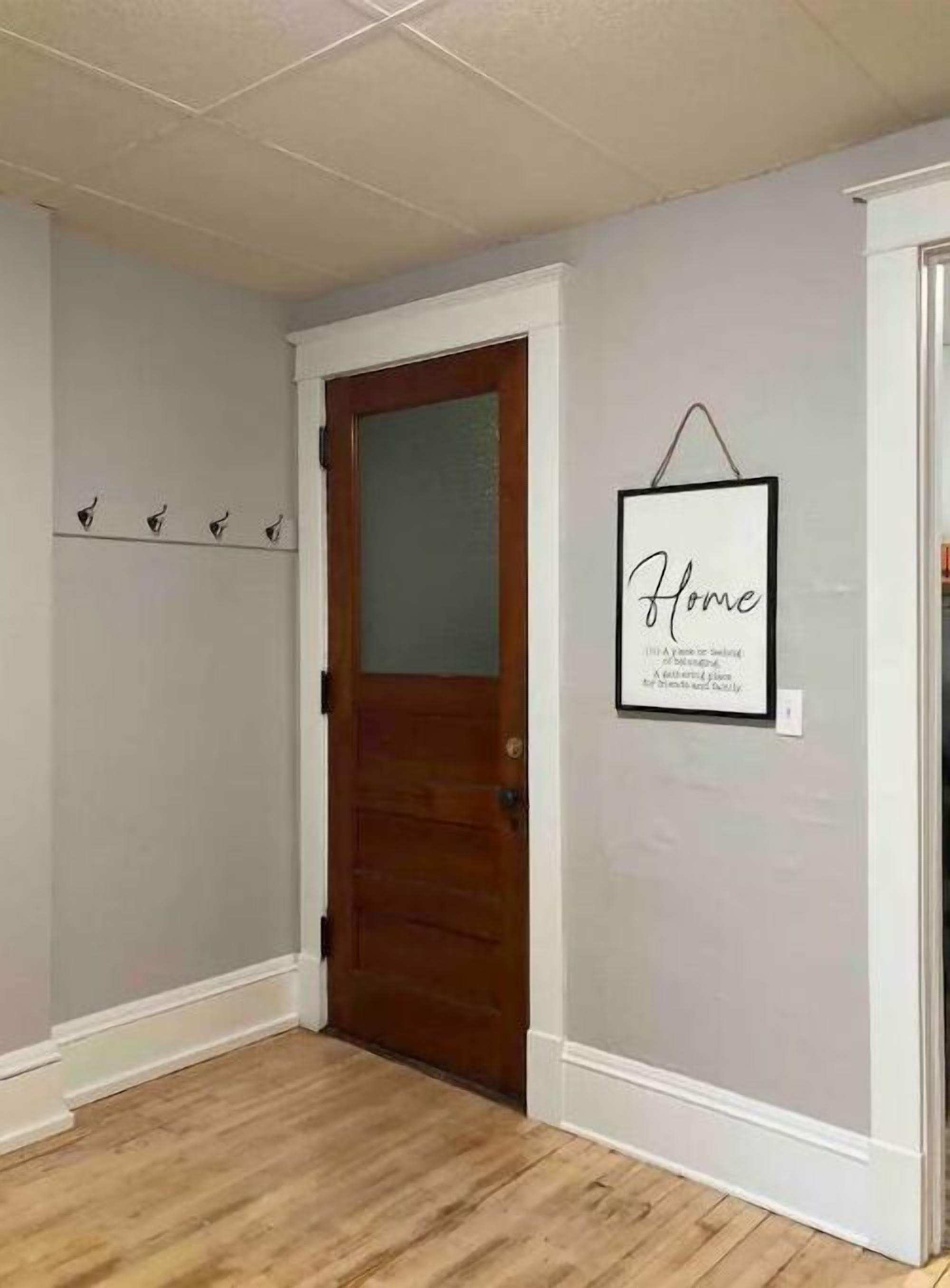 A hallway with a wooden door, a coat rack with coats, and a framed sign on the wall.
