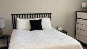 Een bed met een witte spreidek en een donker hoofdbord in een kamer met houten vloer en een witte muur.