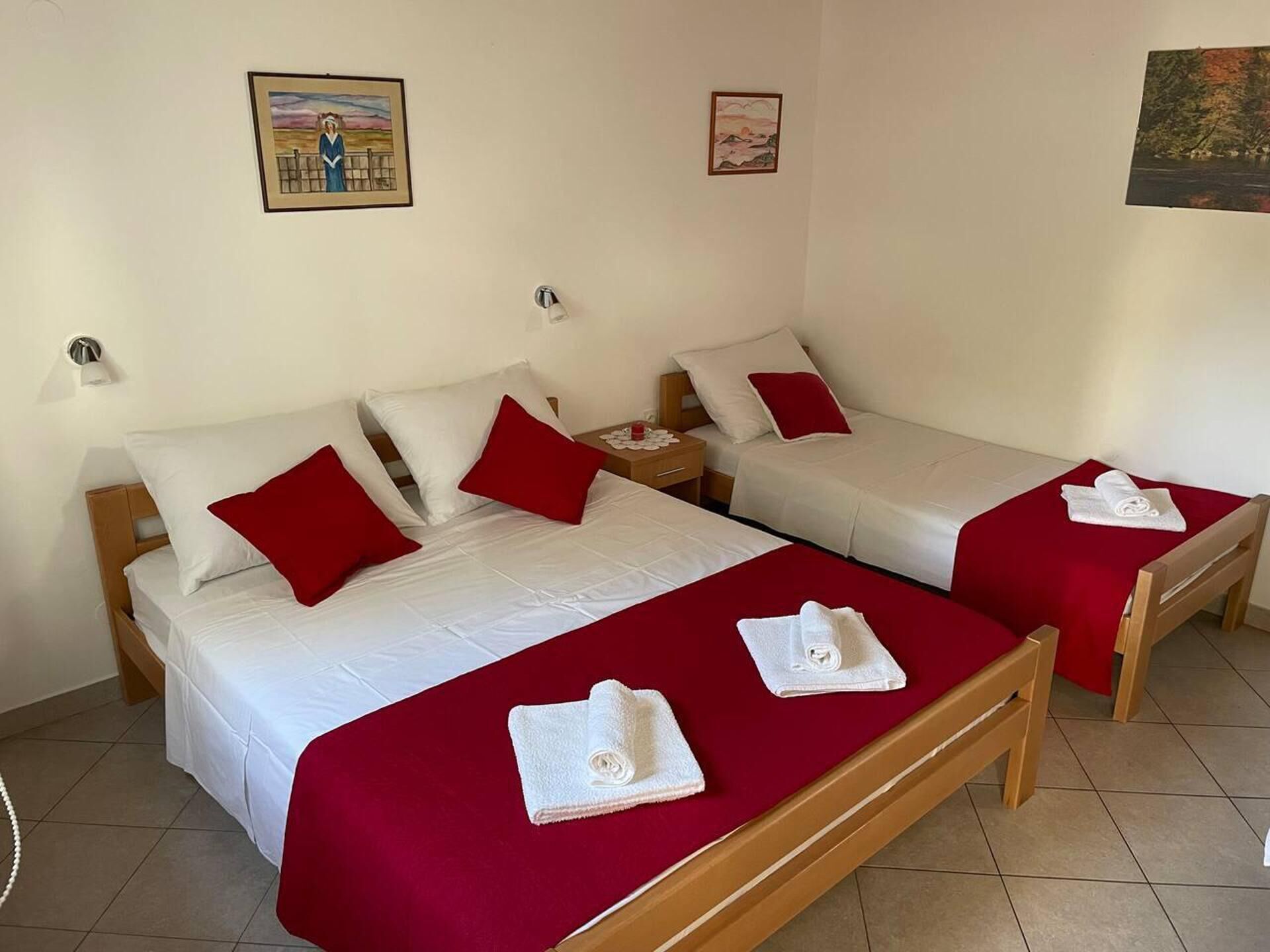 A hotel room with two single beds, each with a red bedspread and white pillows. There are two white towels on the beds.