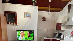 A small kitchen with a dining table set for two, a television on a wooden cabinet, and a red flower vase on the table. - Cosy Apartment Near the Beach in Medulin, Croatia (Medulin)