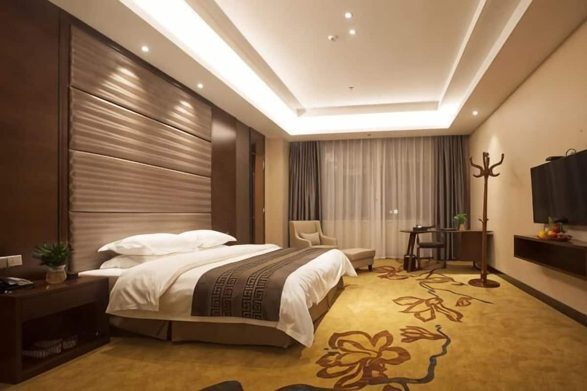 A hotel room with a bed, bedside table, lamp, chair, and a television.