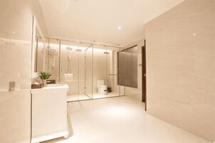 Un baño moderno con cabina de ducha de vidrio, lavamanos blanco y espejo.