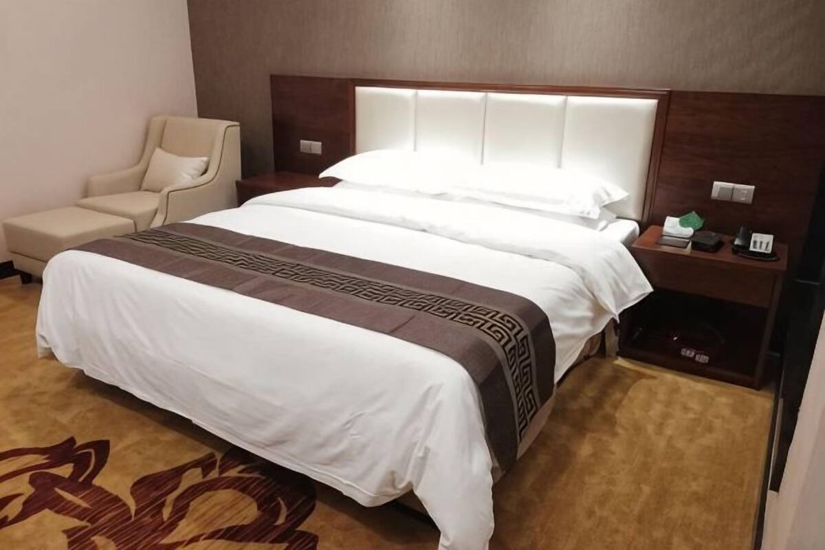 A hotel room with a large bed, a chair, a nightstand, and a carpeted floor.