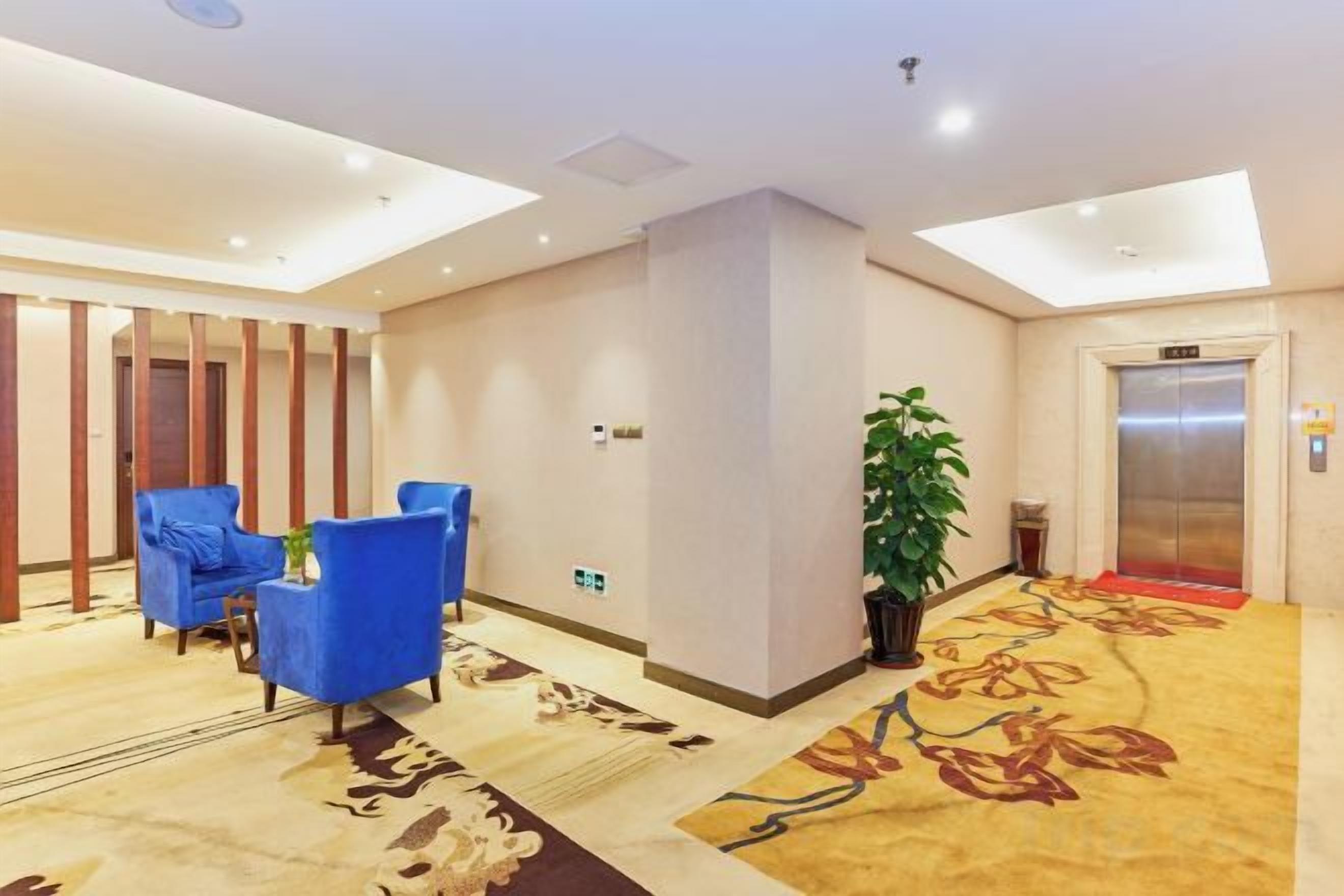 A hotel lobby with a reception desk, blue seating, an elevator, and a patterned carpet.
