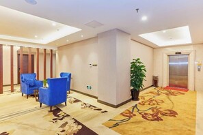 A hotel lobby with a reception desk, blue seating, an elevator, and a patterned carpet. - Shanhai Hotel (Longyan)