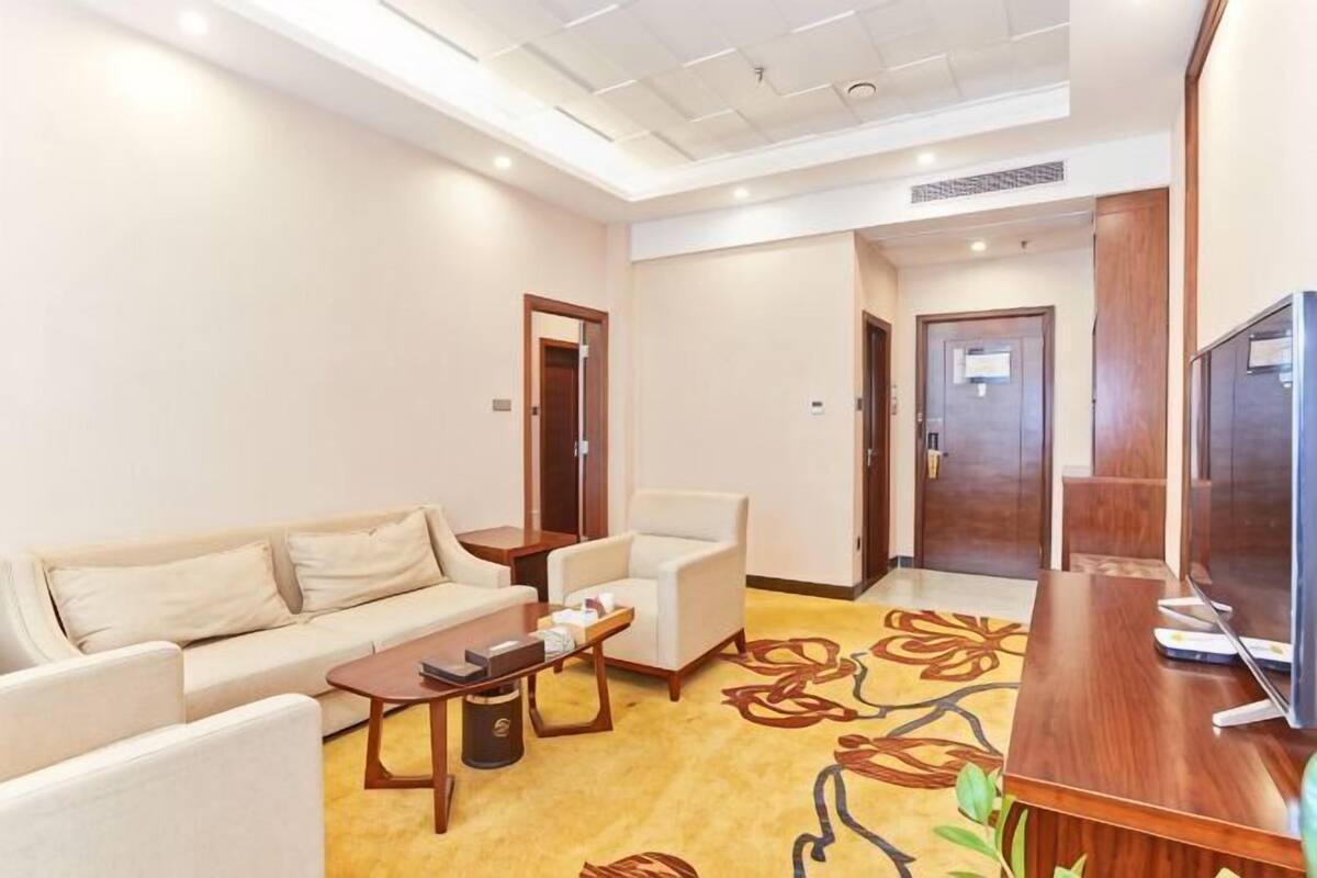 A hotel room with a sofa, armchair, coffee table, TV, and carpet with a floral pattern.