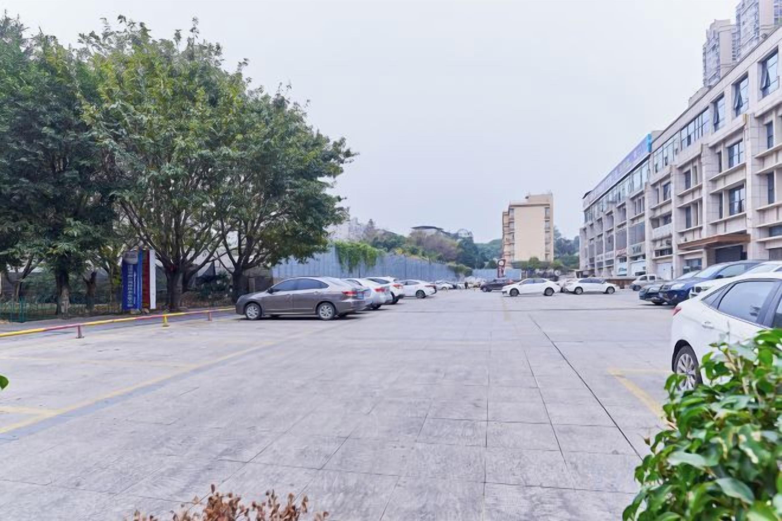 A parking lot with multiple cars, a building with multiple floors, and trees along the left side.