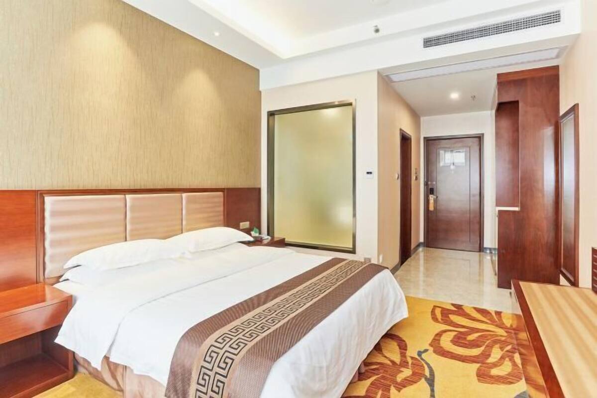 A hotel room with a bed, bedside table, and a large mirror.
