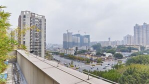 Un edificio alto con varios pisos, un balcón y vistas de un paisaje urbano con otros edificios y grúas de construcción.