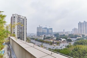 Un edificio alto con varios pisos, un balcón y vistas de un paisaje urbano con otros edificios y grúas de construcción.