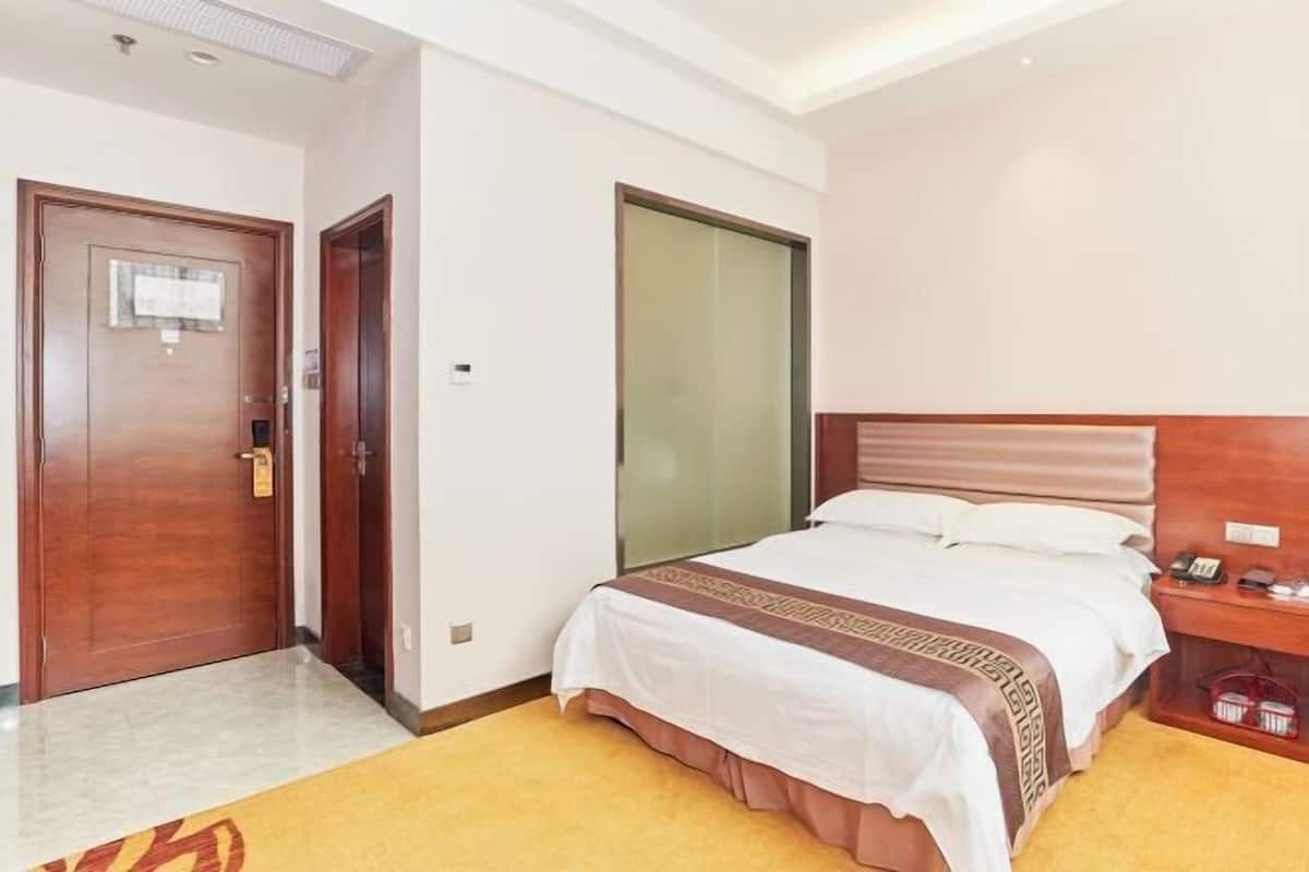 A hotel room with a bed, a wooden headboard, a bedside table with a phone, and a door with a lock.
