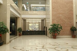 A hotel lobby with a reception desk, potted plants, a marble floor, and a high ceiling with a glass railing. - Shanhai Hotel (Longyan)
