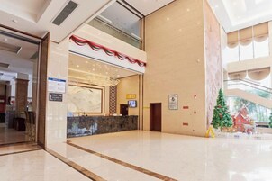 Un vestíbulo de hotel con mostrador de recepción, un árbol de Navidad y un ventanal con vistas a un edificio rojo.