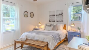 Une chambre à coucher avec un lit, des tables de chevet, un ventilateur de plafond et des œuvres d’art accrochées aux murs.