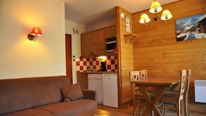 A cozy living area with a sofa, a wooden dining table, and a kitchen with wooden cabinets and a checkered backsplash. - 100m from ski slopes, Ground floor, balcony, 29m², Valloire (Valloire)