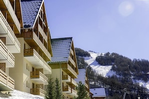 Um hotel de vários andares com varandas, ao fundo uma montanha nevada e um céu claro.