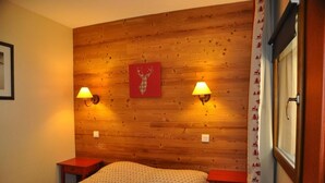 A wooden-paneled room with two bedside lamps, a bed with a patterned bedspread, and a framed picture on the wall. - 100m from ski slopes, Ground floor, balcony, 29m², Valloire (Valloire)