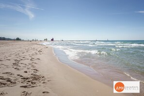 Een strand met voetafdrukken, rustig water en een heldere lucht.