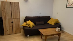 Un soggiorno con un divano marrone scuro, due cuscini gialli, un tavolino in legno e un mobile contenitore in legno con una lampada sopra.