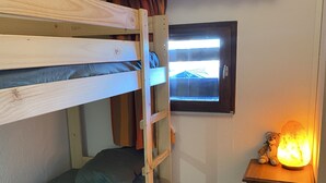Una stanza con un letto a castello, una finestra, un piccolo tavolo con una lampada e un orsacchiotto.