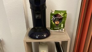 Una macchina da caffè, una confezione di capsule per caffè, un bollitore ed un tostapane su un ripiano di legno.