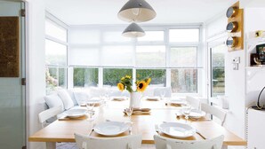 A bright dining area with a large table set for six, white chairs, and a vase of sunflowers. - Secluded rural retreat, close to beach - sleeps 12 (West Sussex)